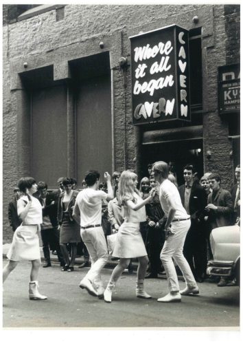 Black and white photo of people dancing outside The Cavern Club in Liverpool with a crowd watching under the sign reading "Where it all began."