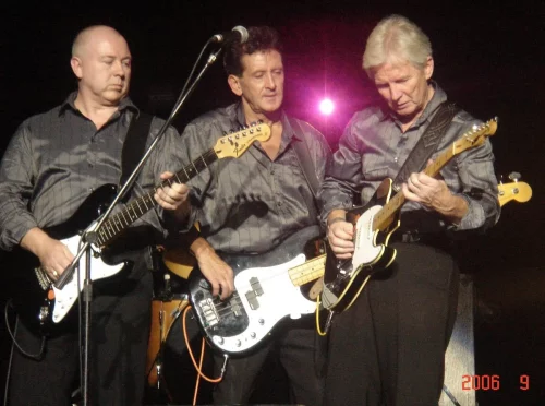 Colour photo of three members of The Searchers playing guitars on stage during a live performance in 2006.